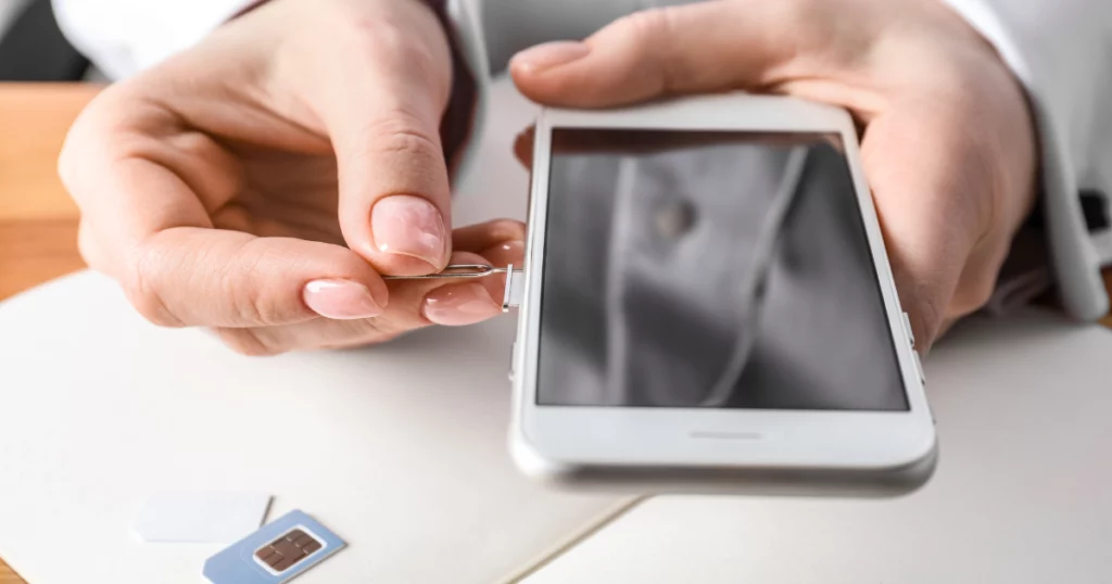 photo d'une main en train d'enlever une carte sim d'un téléphone pour en changer